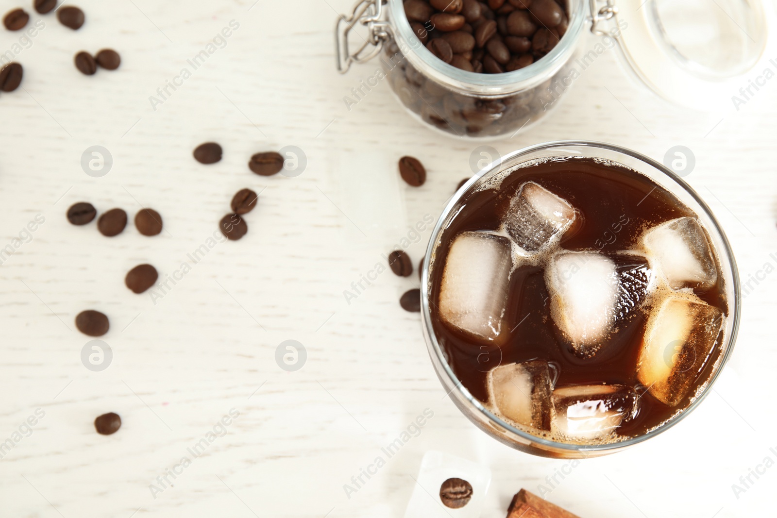 Photo of Glass of coffee drink with ice cubes on light table, flat lay. Space for text