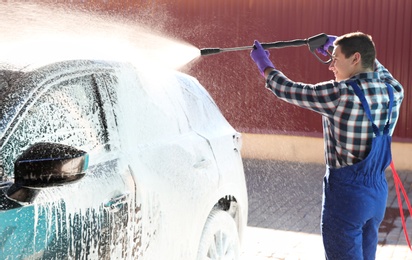 Worker cleaning automobile with high pressure water jet at car wash