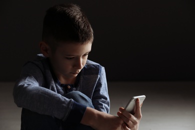 Photo of Upset boy with smartphone sitting indoors. Space for text