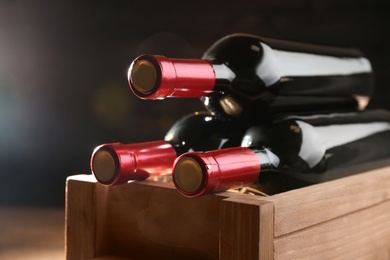 Photo of Wooden crate with bottles of wine on dark background, closeup