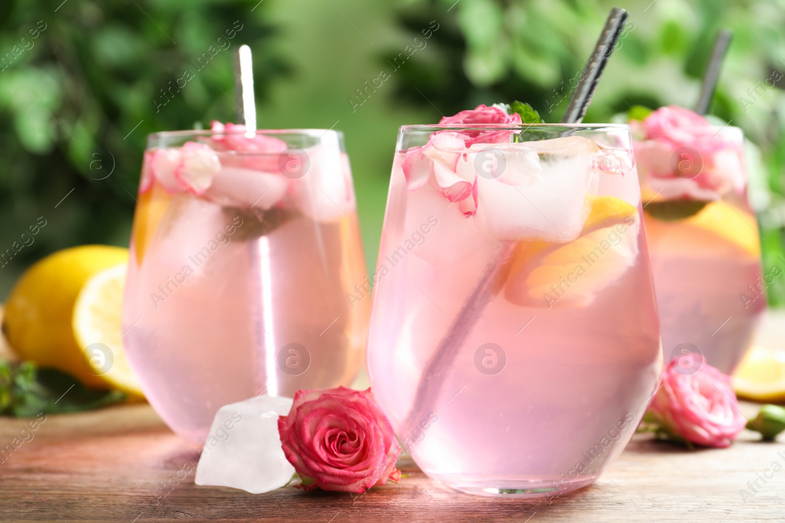 Photo of Delicious refreshing drink with rose flowers and lemon slices on wooden table, closeup