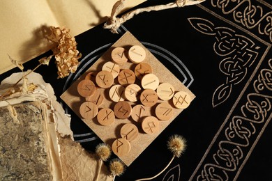 Many wooden runes, old books and dried flowers on divination mat, flat lay