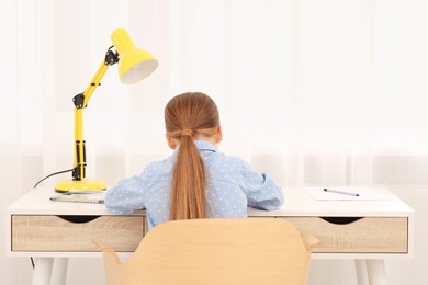 Photo of Little girl drawing at desk in room, back view. Home workplace