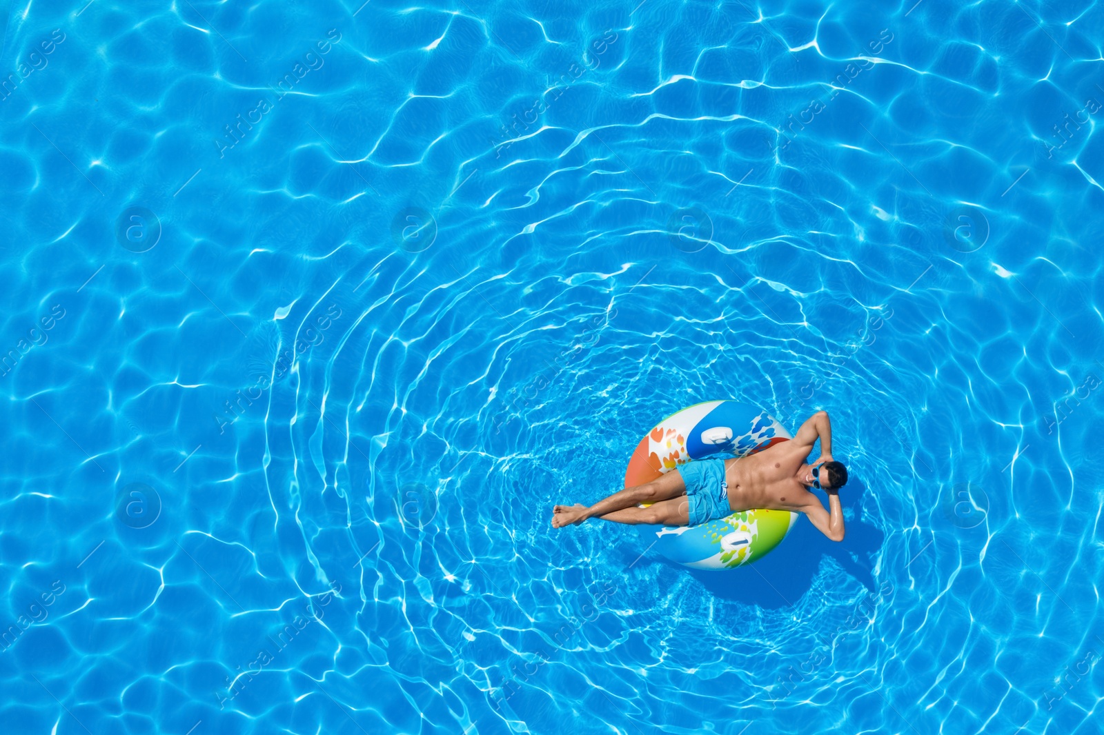 Image of Young man with inflatable ring in swimming pool, top view. Space for text