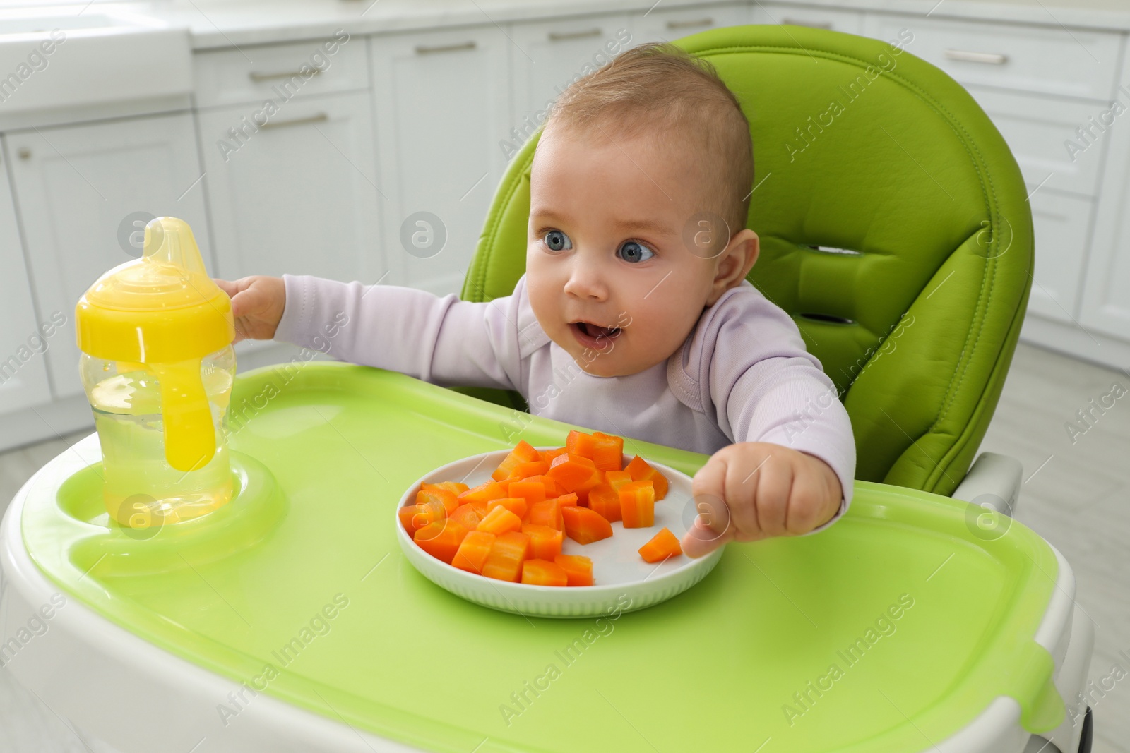 Photo of Cute little baby eating carrot at home, focus on plate