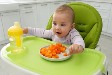 Photo of Cute little baby eating carrot at home, focus on plate