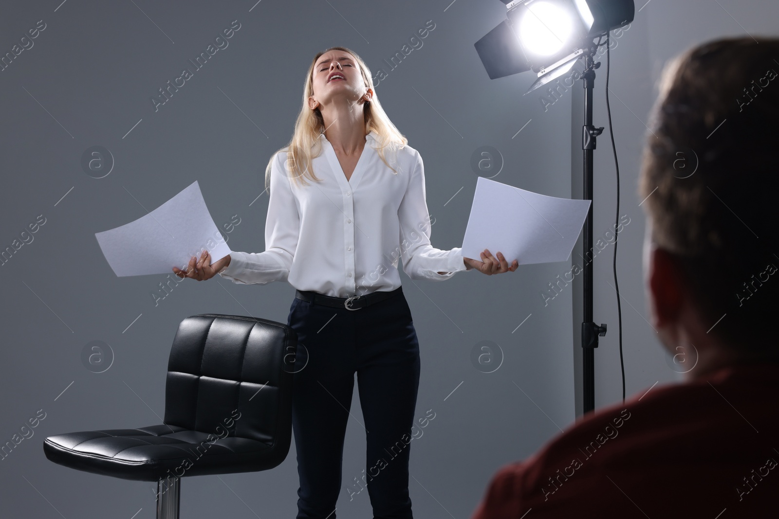 Photo of Emotional woman with script performing in front of casting director against grey background in studio