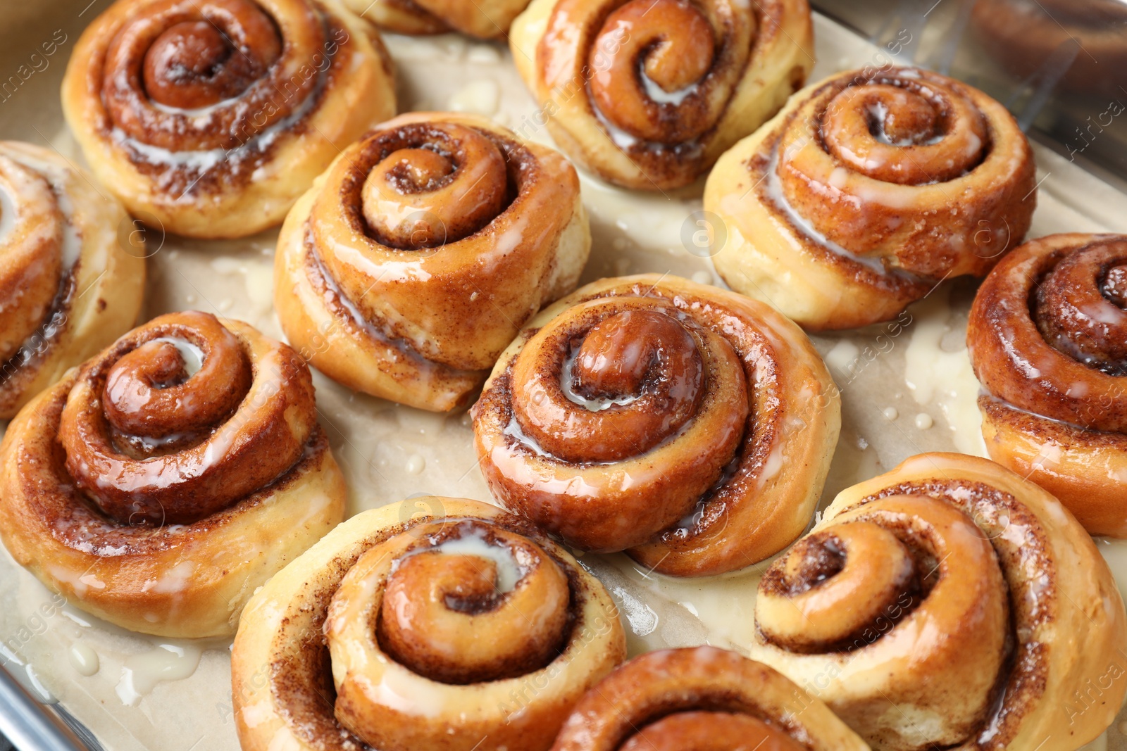 Photo of Tasty cinnamon rolls with cream on parchment paper, closeup