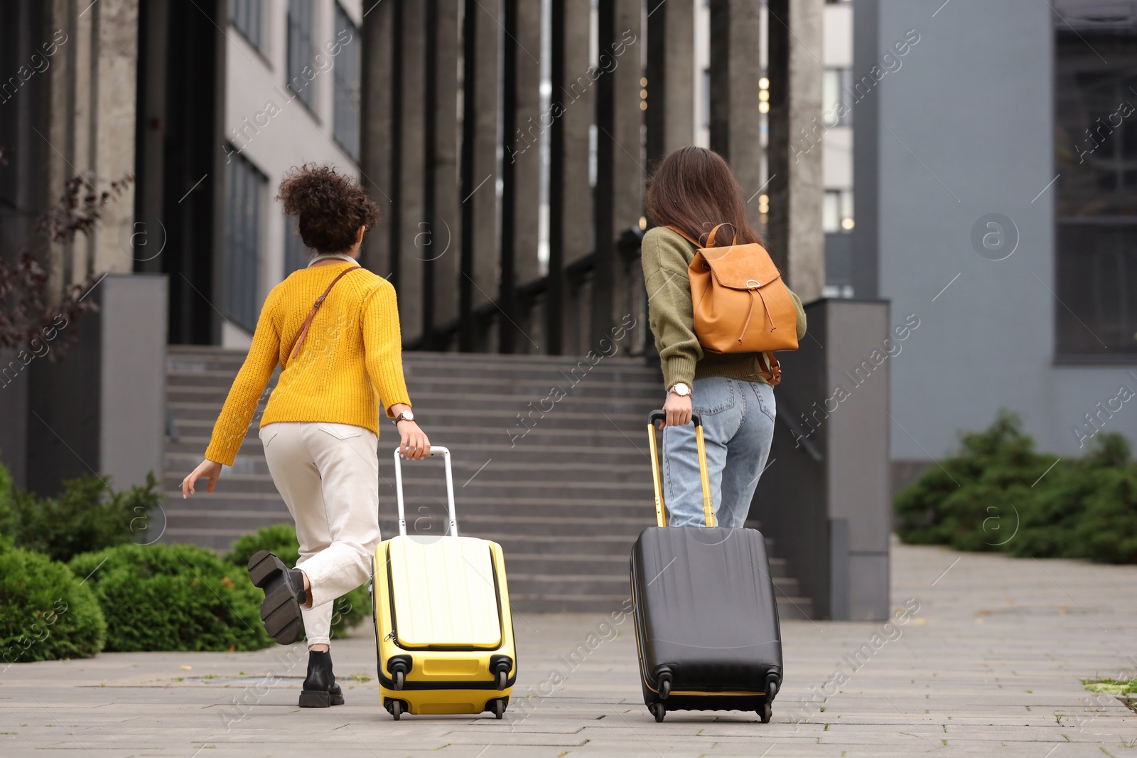 Photo of Being late. Women with suitcases running towards building outdoors, back view