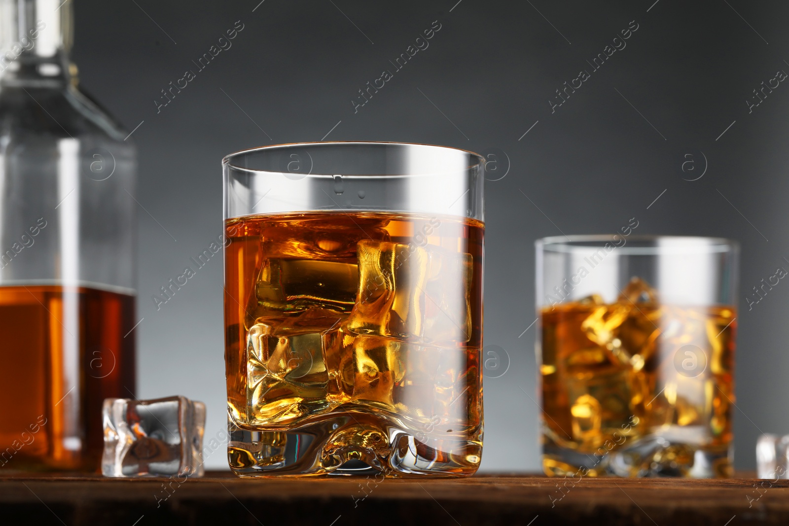 Photo of Whiskey with ice cubes in glasses on table against grey background, closeup