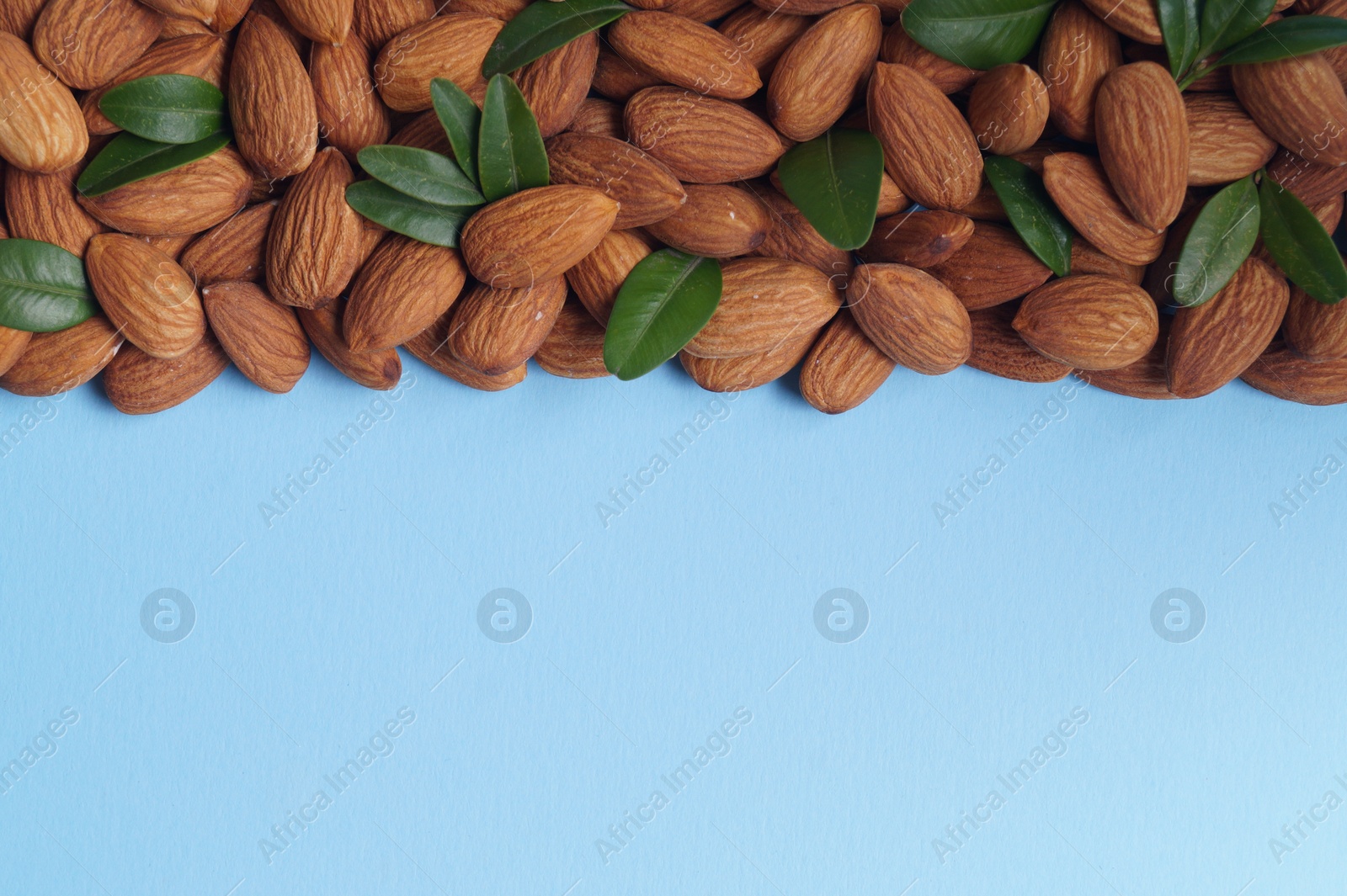 Photo of Delicious almonds and fresh leaves on light blue background, flat lay. Space for text
