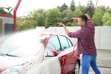 Young man cleaning vehicle with high pressure foam jet at self-service car wash