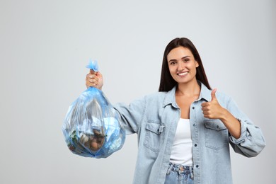 Woman holding full garbage bag on light background