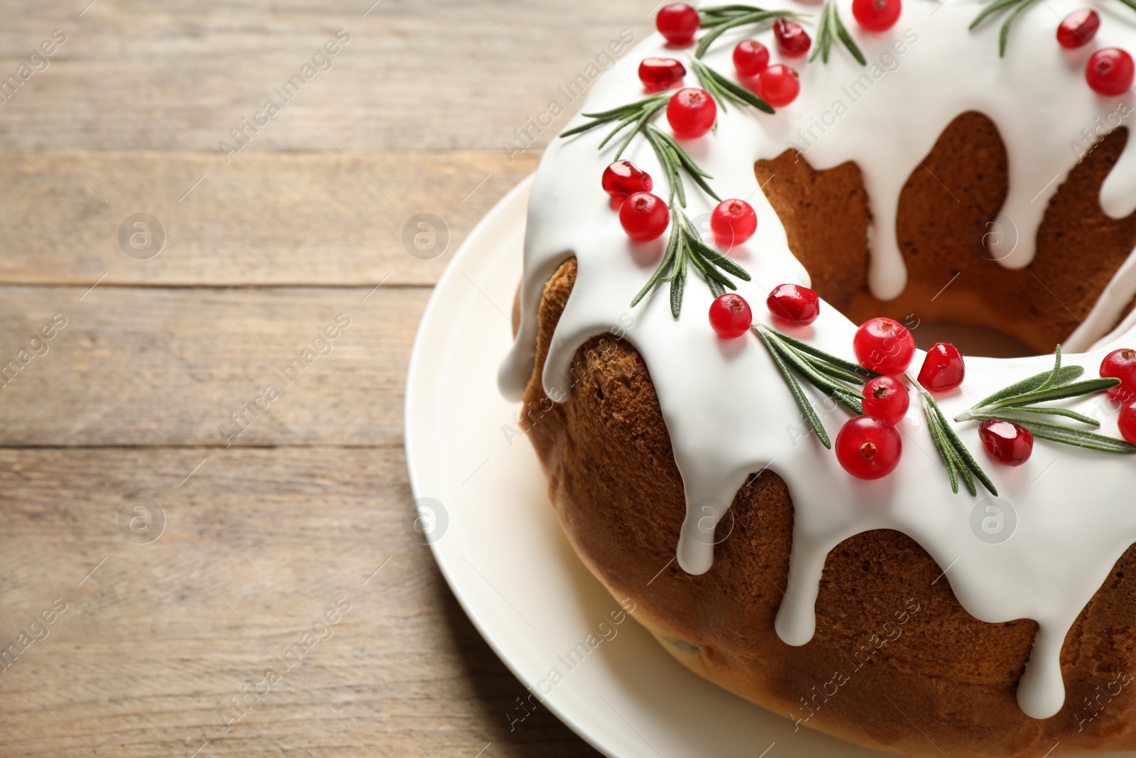 Photo of Traditional Christmas cake decorated with glaze, pomegranate seeds, cranberries and rosemary on wooden table, closeup. Space for text