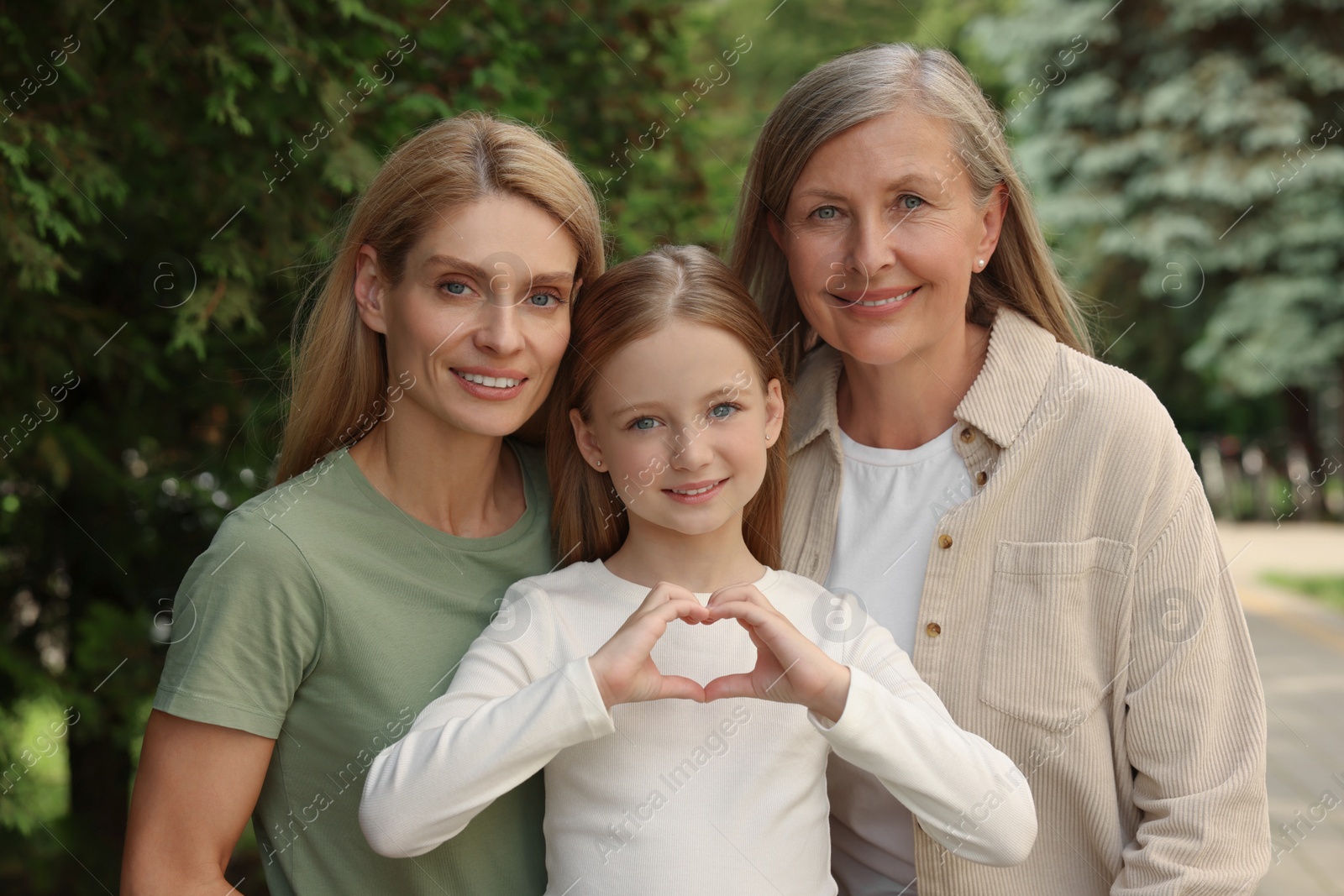 Photo of Three generations. Happy grandmother, her daughter and granddaughter making heart with hands outdoors