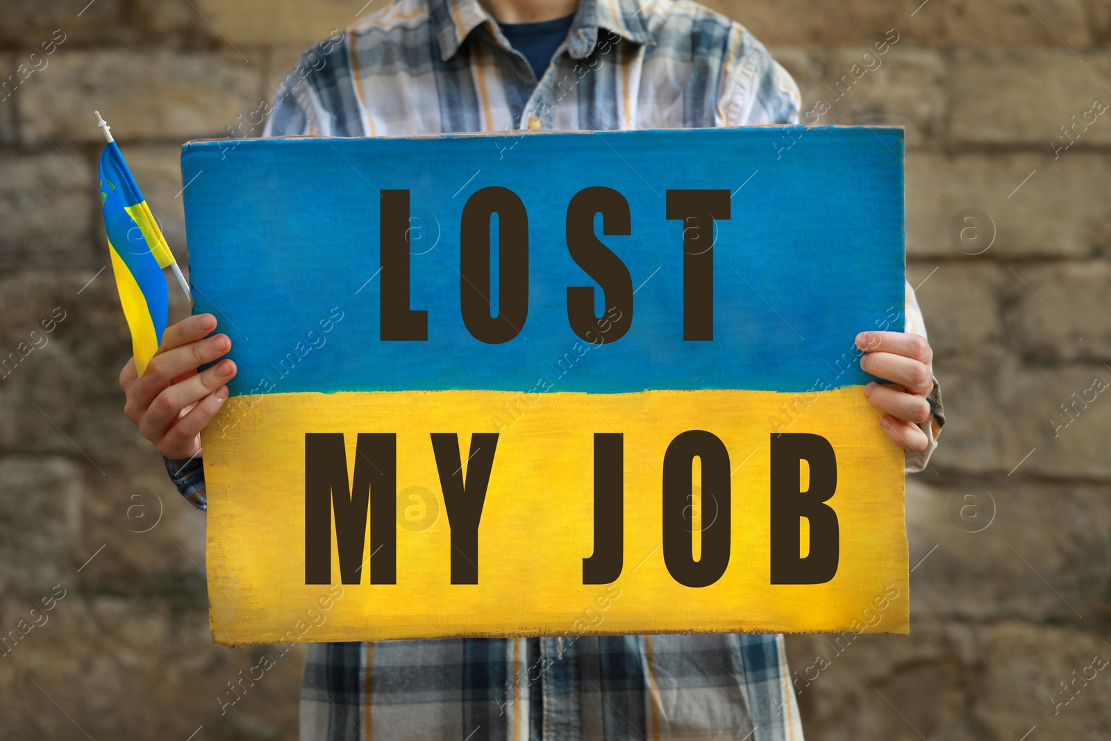 Image of Unemployed due to war. Woman holding poster in colors of Ukrainian flag and phrase Lost My Job against brick wall, closeup