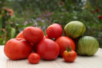 Photo of Many different ripe tomatoes on white wooden table in garden