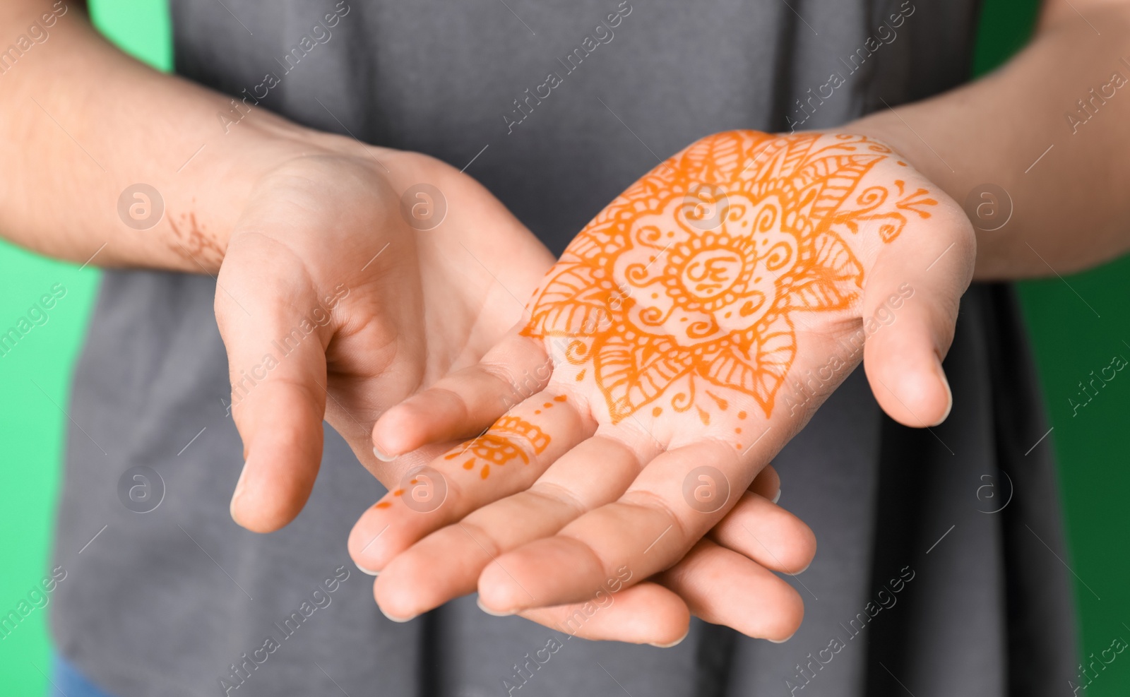 Photo of Woman with henna tattoo on palm against green background, closeup. Traditional mehndi ornament