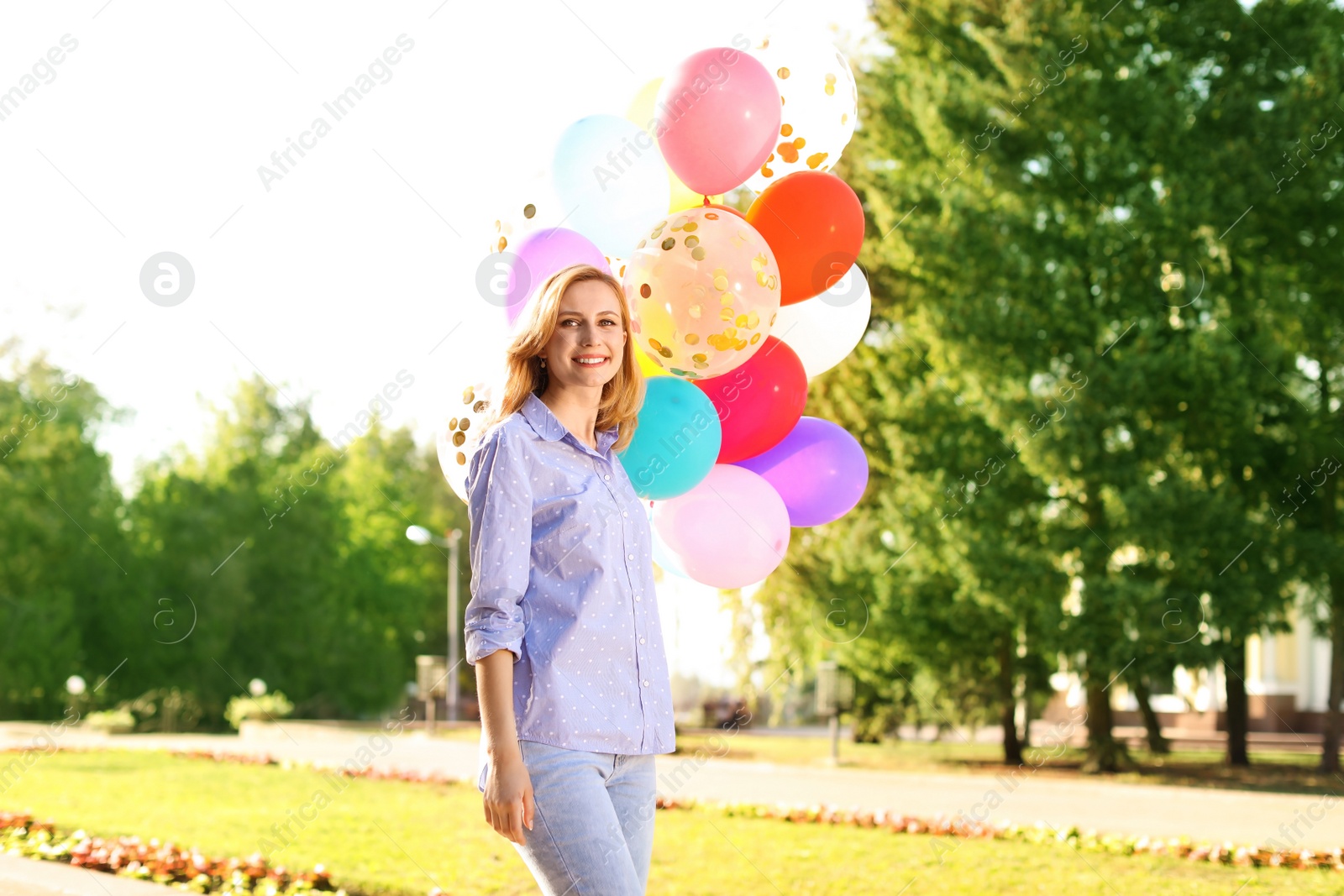 Photo of Young woman with colorful balloons outdoors on sunny day