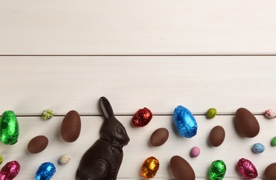 Dark chocolate Easter bunny and eggs on white wooden table, flat lay. Space for text