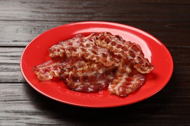 Plate with fried bacon slices on wooden table, closeup