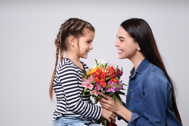 Photo of Happy woman with her cute daughter and bouquet of beautiful flowers on light grey background. Mother's day celebration