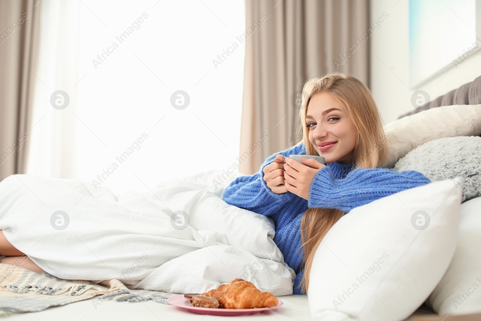 Photo of Beautiful young woman lying with breakfast in bed at home. Winter atmosphere