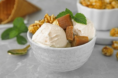 Photo of Bowl of delicious ice cream with caramel candies, popcorn and mint on light grey marble table, closeup