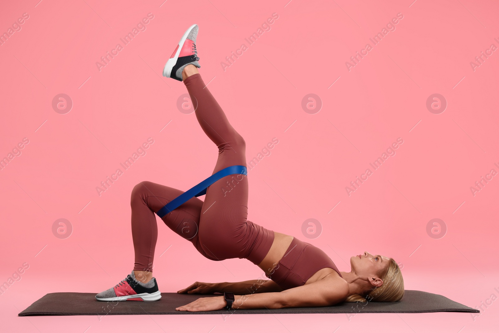 Photo of Woman exercising with elastic resistance band on fitness mat against pink background