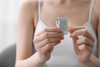 Woman pulling condom out from package indoors, closeup. Safe sex