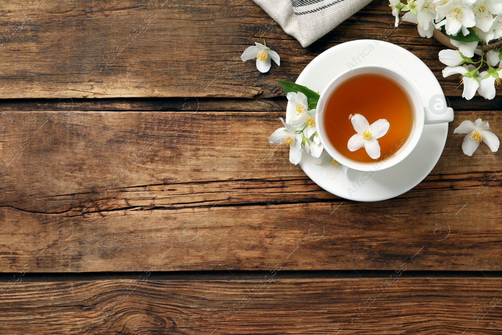 Photo of Cup of aromatic jasmine tea and fresh flowers on wooden table, flat lay. Space for text
