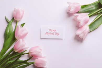 Photo of Beautiful tulips and greeting card with words "Happy Mother's Day" on light background, top view