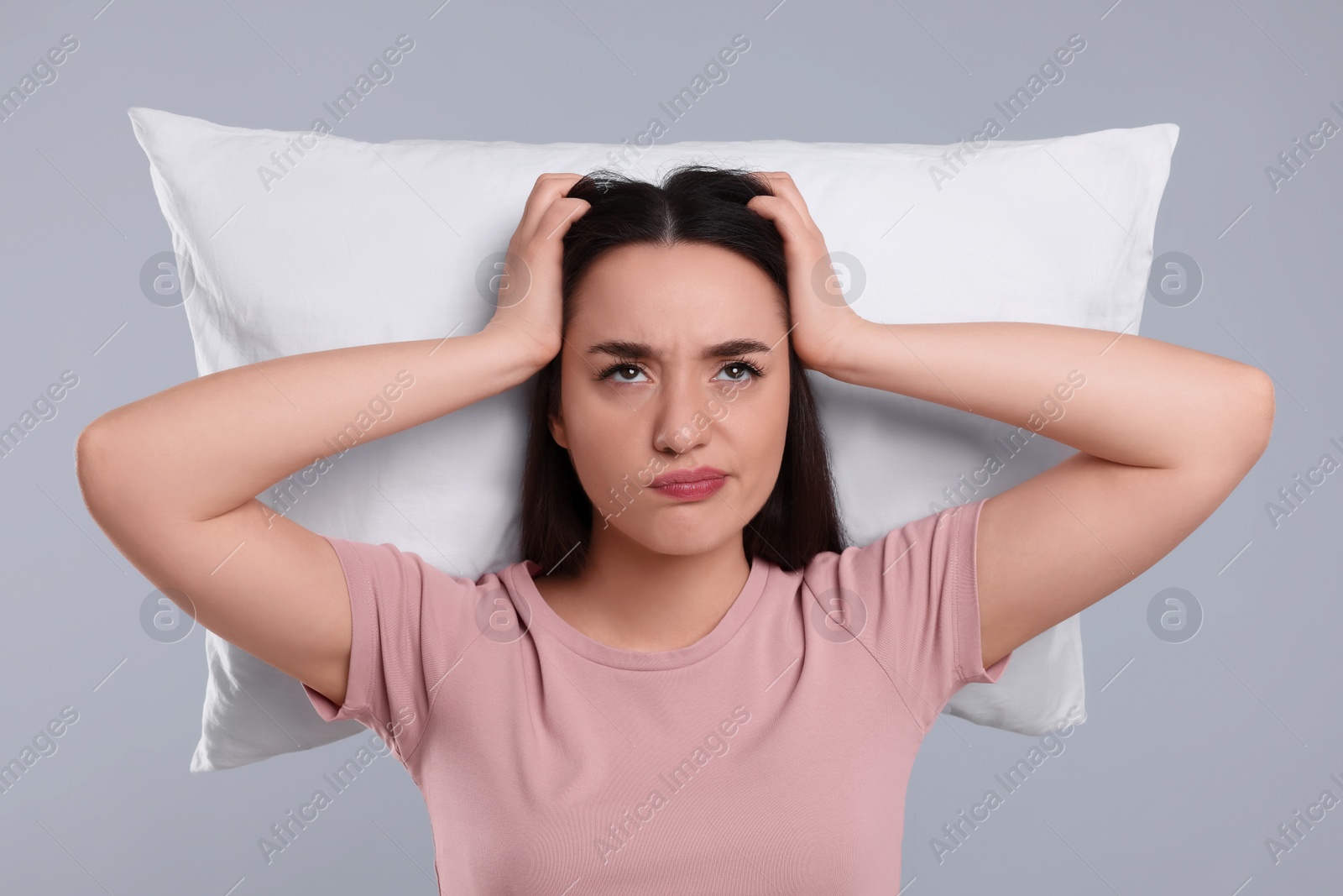 Photo of Tired young woman with pillow on light grey background. Insomnia problem