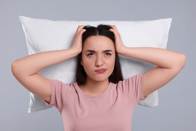 Photo of Tired young woman with pillow on light grey background. Insomnia problem