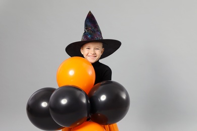 Photo of Cute little girl with balloons wearing Halloween costume on grey background