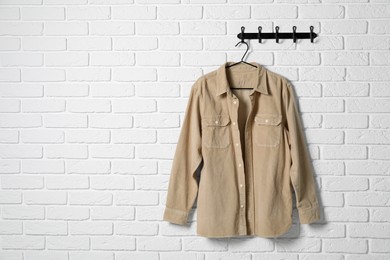 Hanger with beige shirt on white brick wall, space for text