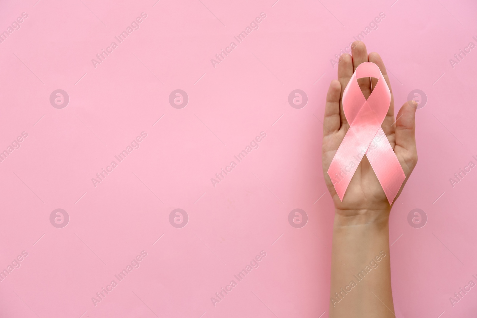 Photo of Woman holding symbolic ribbon of breast cancer awareness on color background, top view. Gynecological care