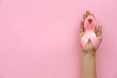 Photo of Woman holding symbolic ribbon of breast cancer awareness on color background, top view. Gynecological care