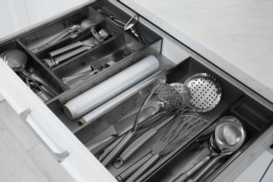 Photo of Open drawer with stainless steel utensil set, closeup. Order in kitchen