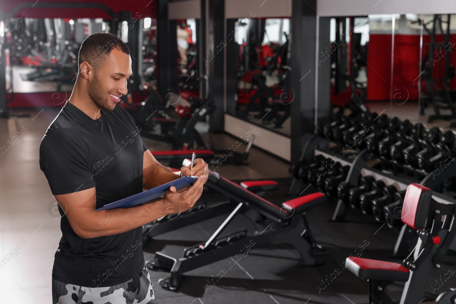 Photo of Happy trainer writing down workout plan in modern gym, space for text