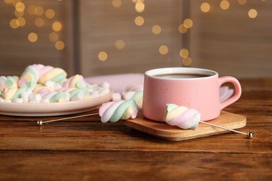 Cup of delicious hot chocolate and marshmallows on wooden table against festive lights