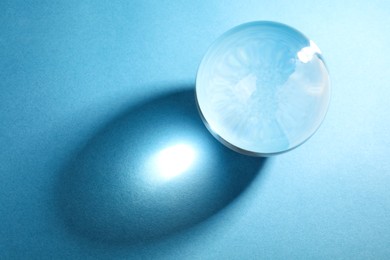 Photo of Transparent glass ball on light blue background, top view. Space for text