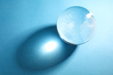 Transparent glass ball on light blue background, top view. Space for text