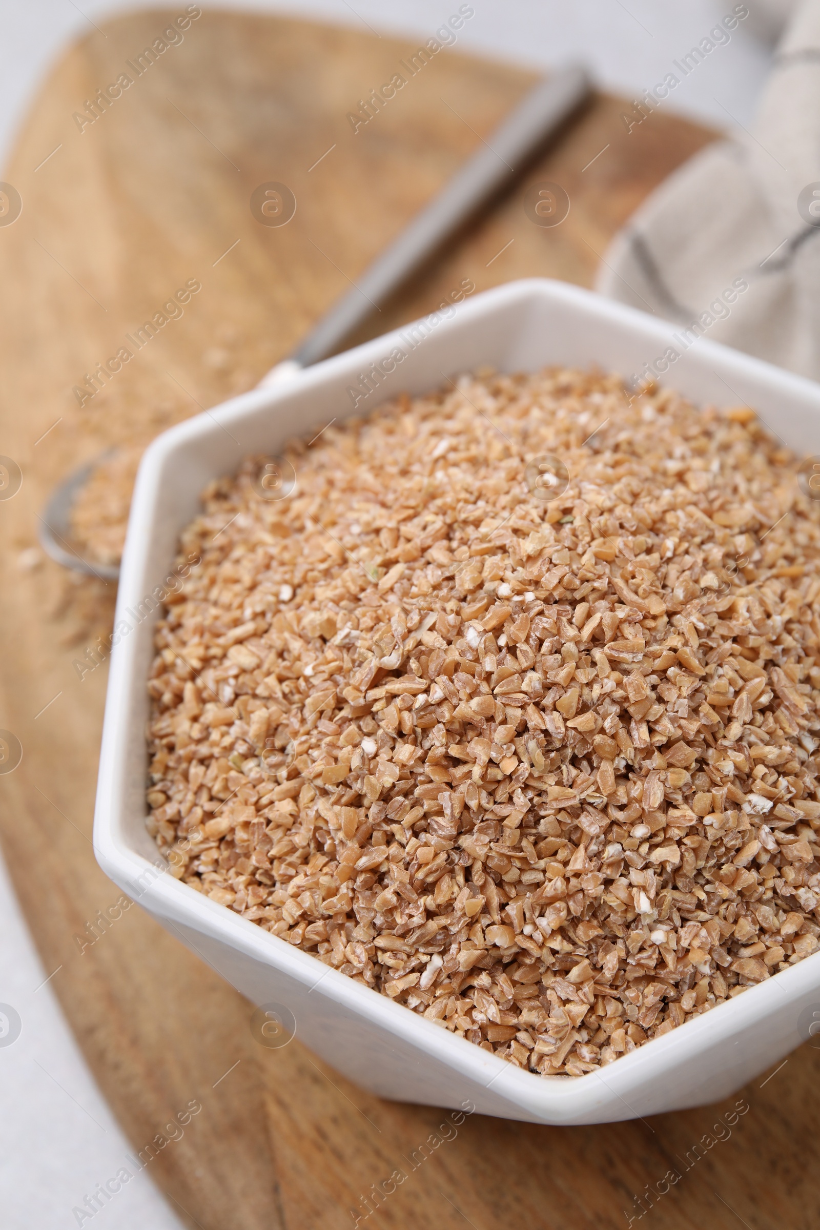 Photo of Dry wheat groats in bowl on light table, closeup