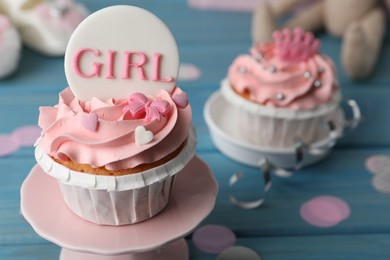 Photo of Delicious cupcake with pink cream and Girl topper for baby shower on light blue wooden table, closeup