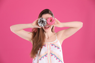 Beautiful young woman with donuts on pink background