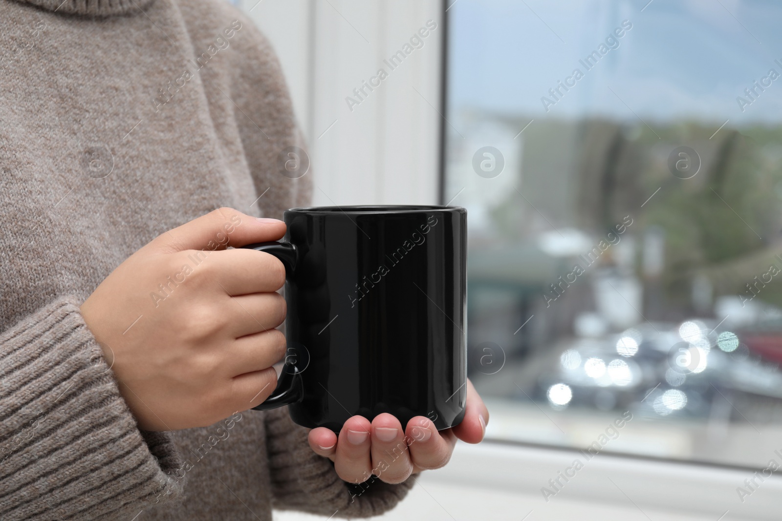 Photo of Woman holding black mug indoors, closeup. Mockup for design