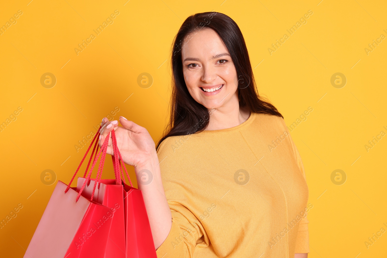 Photo of Beautiful overweight woman with shopping bags on yellow background