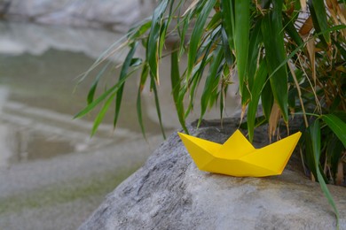 Beautiful yellow paper boat on stone and green plant leaves outdoors, space for text