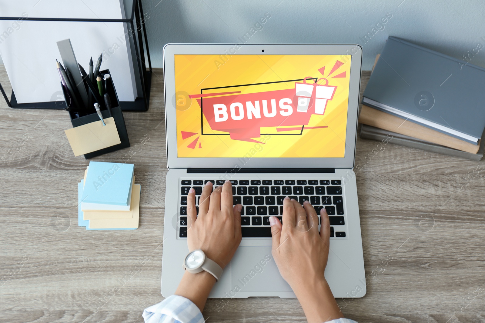 Image of Bonus gaining. Woman using laptop at wooden table, above view. Illustration of gift box and word on device screen